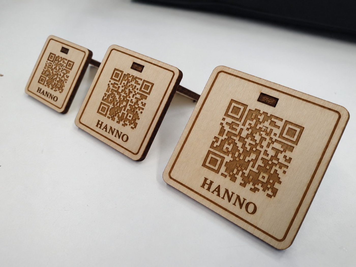 Drie co:carte QR-standaarden in hout, elk met naam en QR-code gegraveerd, in oplopende maat